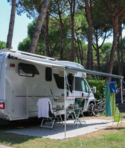 Camper in campeggio sotto gli alberi con tenda e sedie.