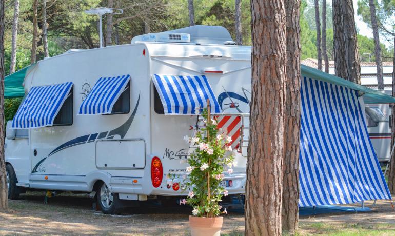 White camper with blue striped awnings at a campsite among trees.