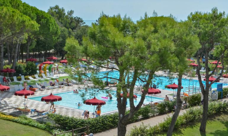 Piscina all'aperto con ombrelloni rossi e alberi verdi.