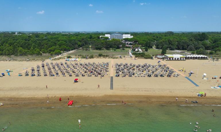 Crowded beach with umbrellas, calm sea, and vegetation in the background.
