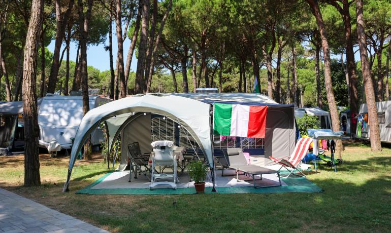Camping with Italian flag, chairs, and loungers under trees.