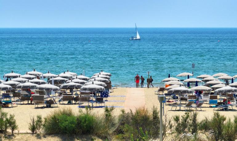 Sandstrand mit Sonnenschirmen und Segelboot auf dem Meer.