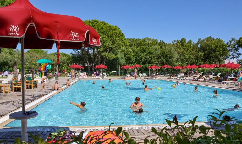 Udendørs pool med røde parasoller og folk, der har det sjovt.