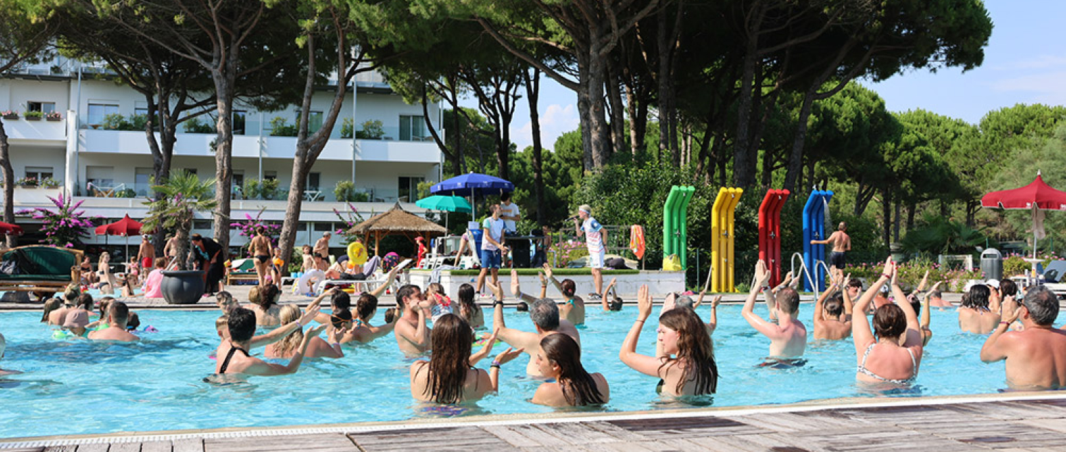 Folk laver vandgymnastik i udendørs pool, omgivet af træer.